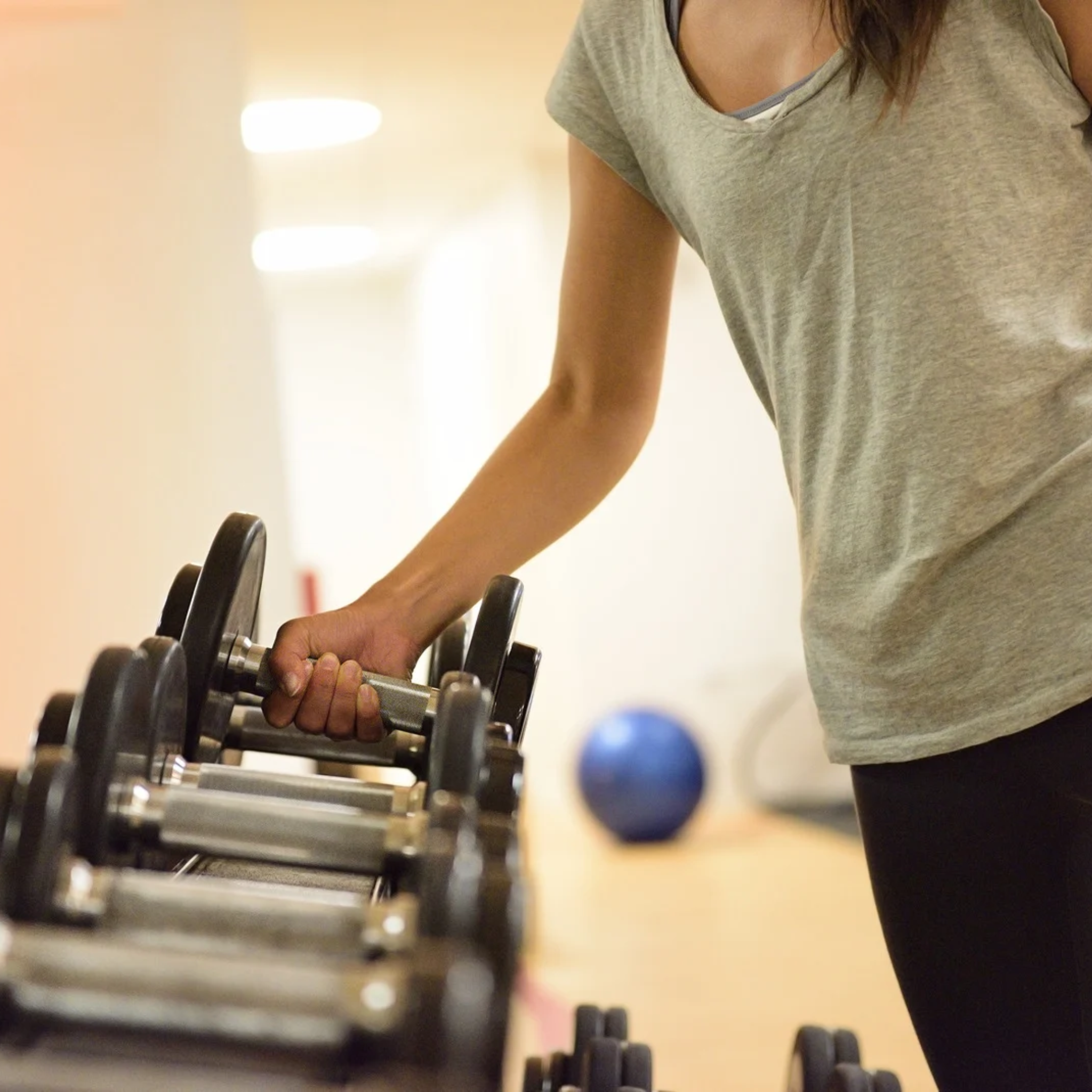 Vrouw pakt een dumbbell uit het rek voor krachttraining tegen buikvet